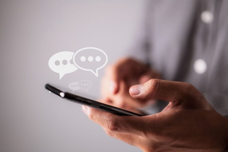Close-up of a person typing on a smartphone with chat bubbles, symbolizing SMS or text message communication.