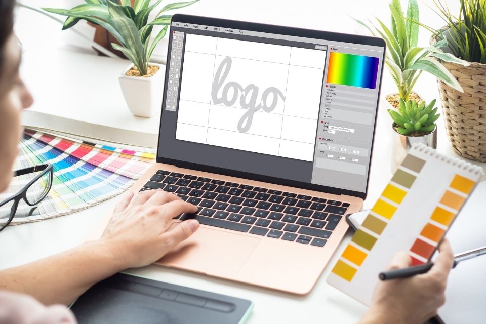 A logo designer working on a laptop, sketching a logo on screen while holding a color palette