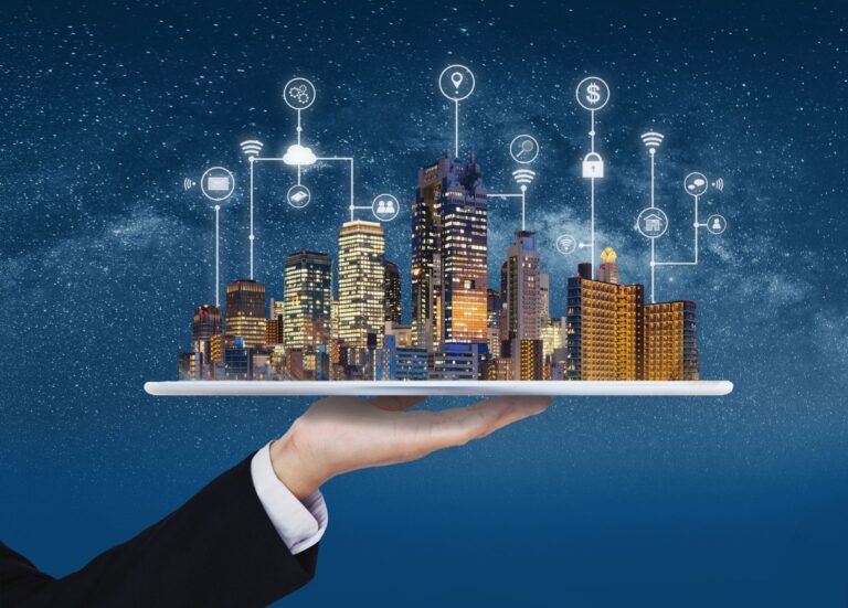 A hand in a suit holding a tablet, with a brightly lit miniature city skyline resting on top against a starry night sky