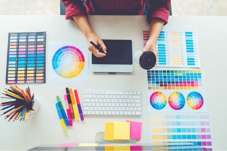 Top view of graphic designer's workspace with color palettes, digital tablet, and tools for creative design projects