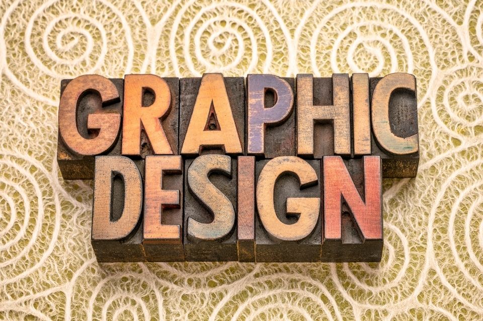 Wooden letterpress blocks spelling 'GRAPHIC DESIGN' on a textured background.