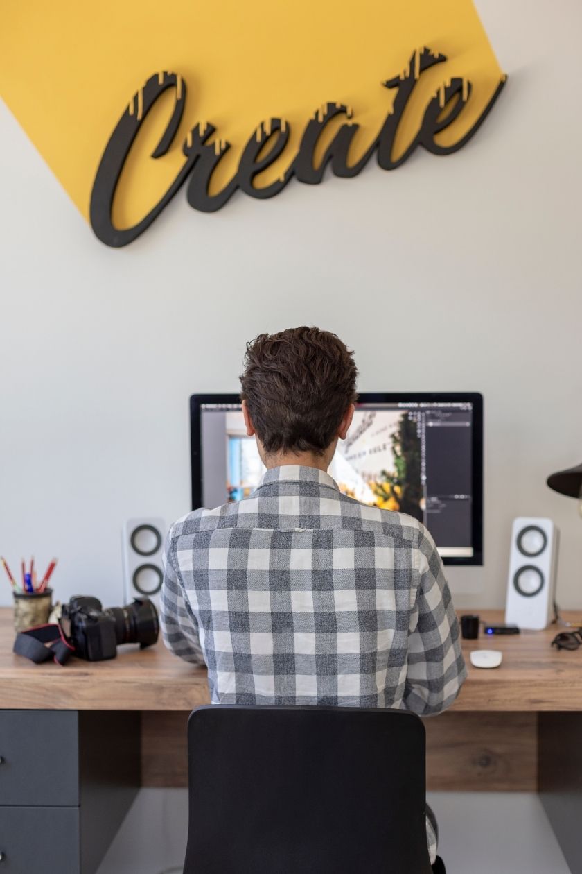A person in a plaid shirt working at a computer, with the word 'Create' on the wall above