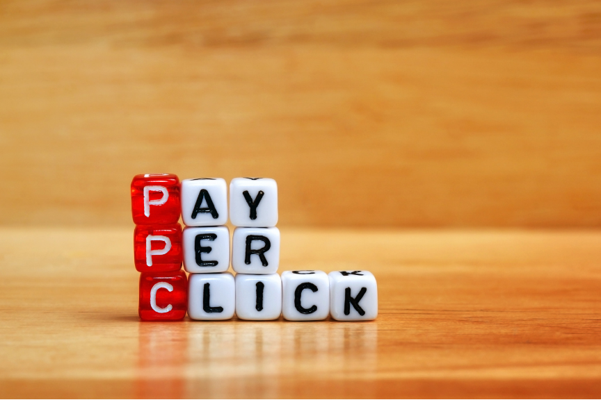Red and white letter beads spelling out 'PAY PER CLICK' on a wooden surface