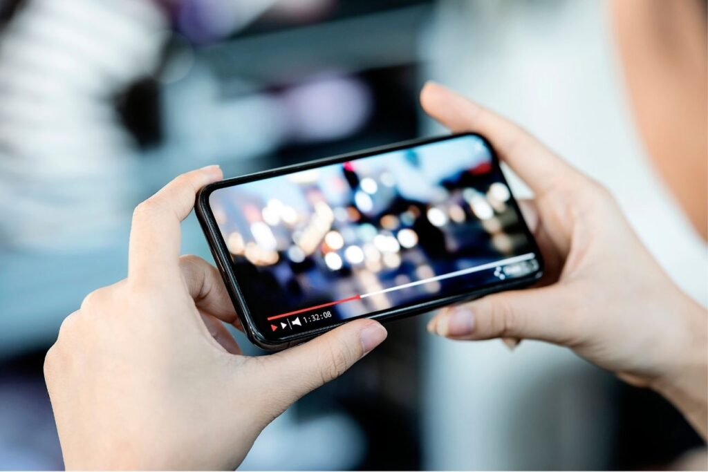 Close-up of hands holding a smartphone while streaming a video, symbolizing mobile video consumption and digital media engagement