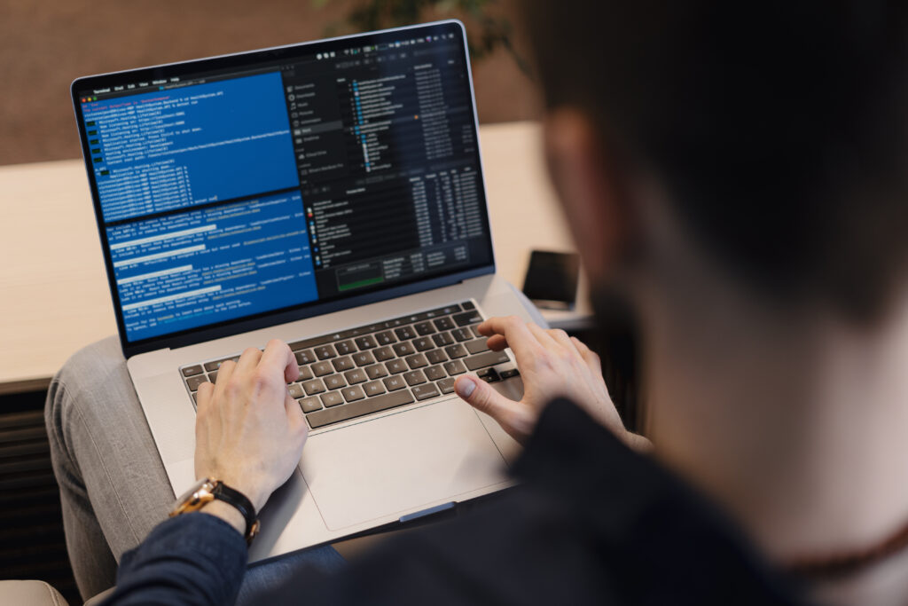 A developer typing on a laptop with a command-line interface on the screen