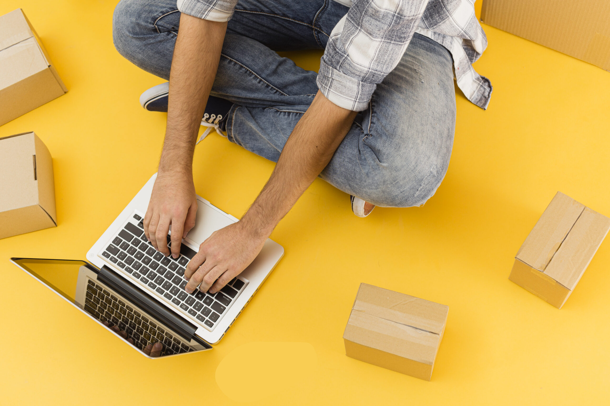 Person using a laptop surrounded by cardboard boxes, symbolizing online store management and WooCommerce-based eCommerce operations
