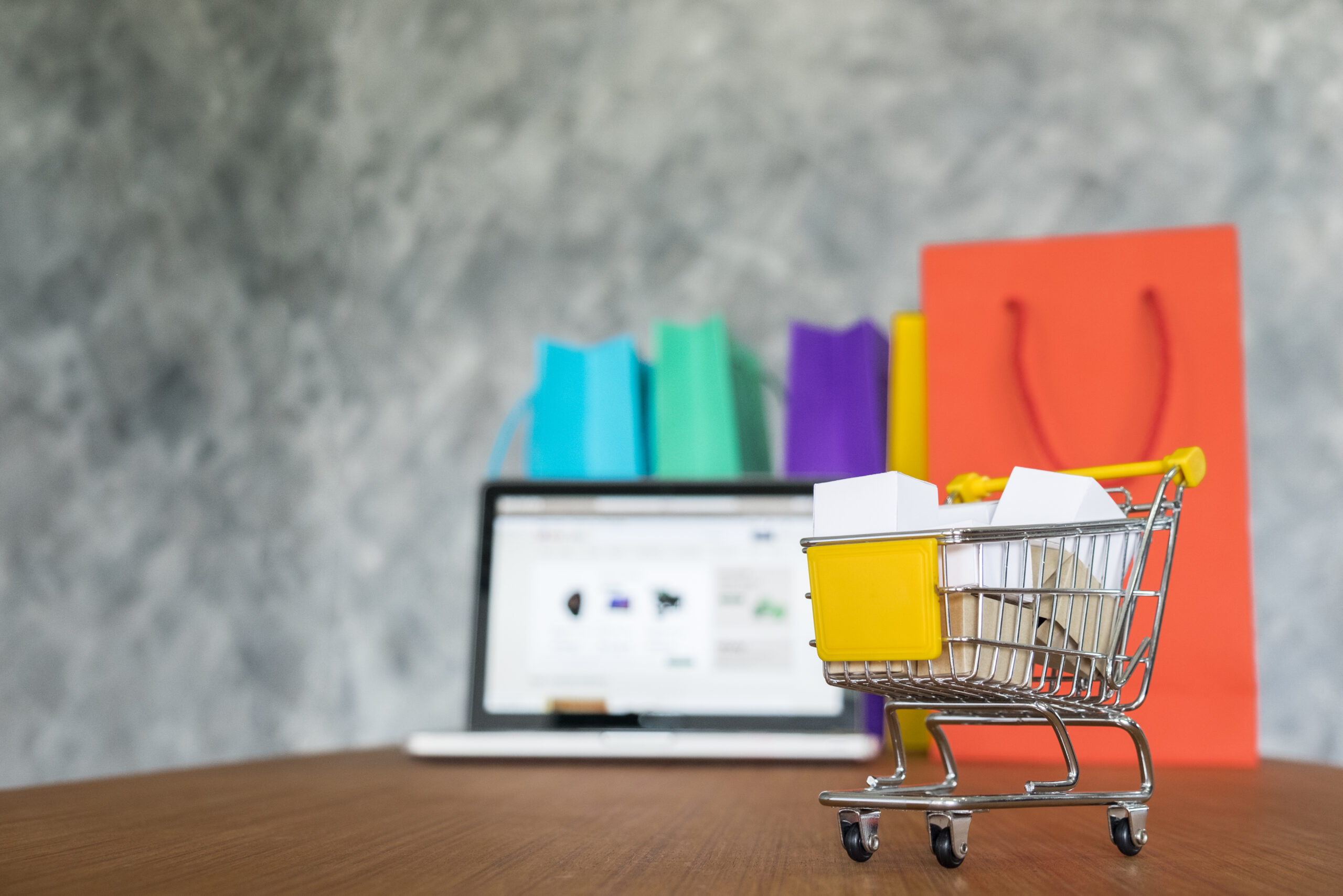 A miniature shopping cart filled with packages in front of a laptop, symbolizing a successful online shopping experience