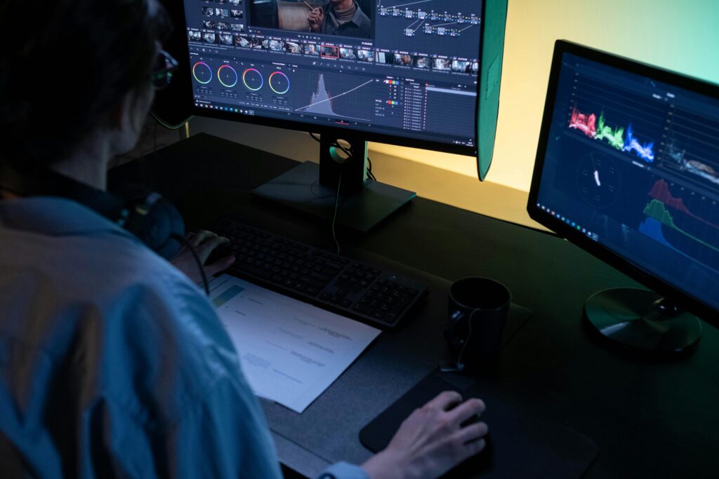 A video editor at a dual-monitor workstation, performing detailed color grading and analysis with professional software and video scopes.