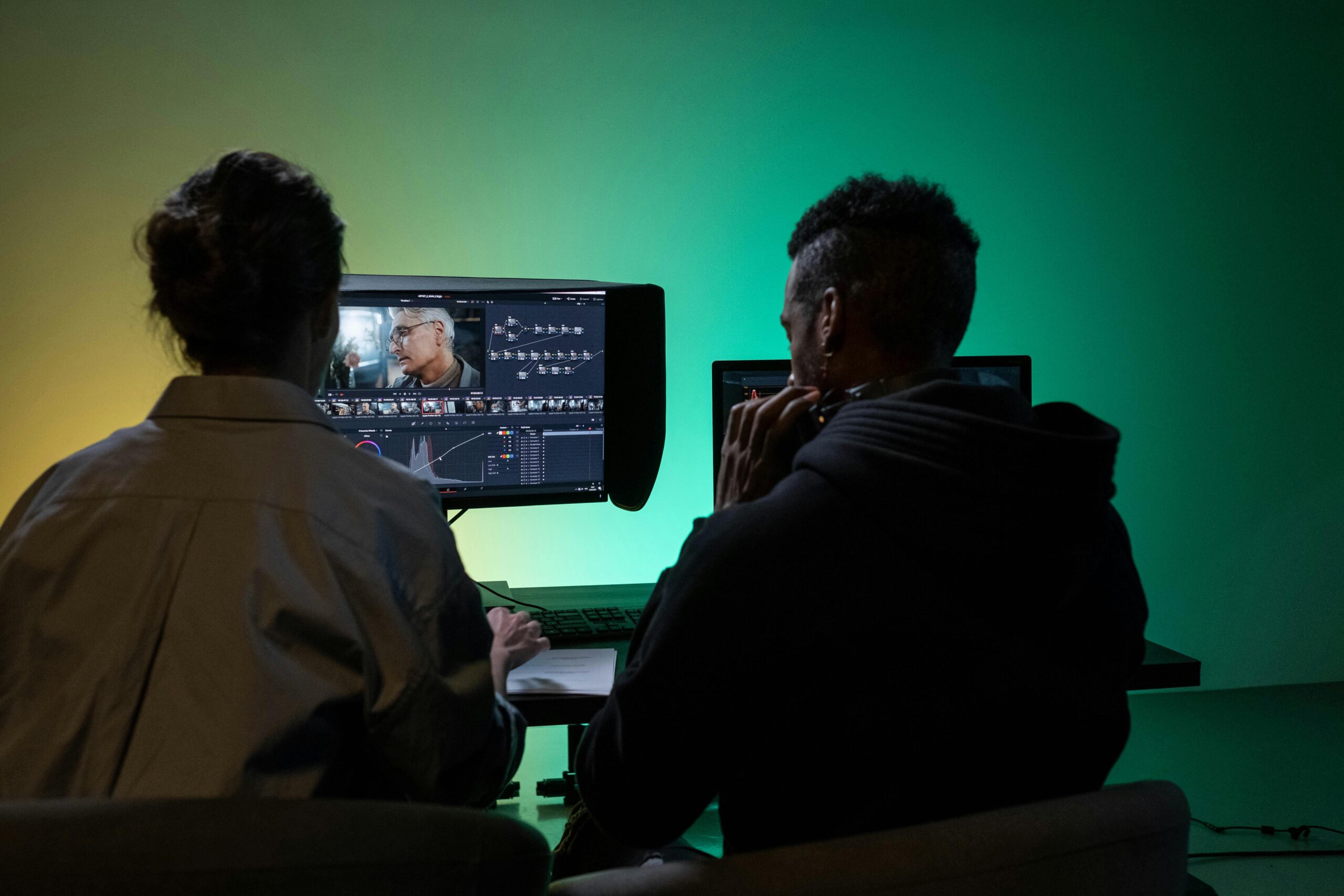 Two video editors collaborating on a project in a studio with green and yellow ambient lighting