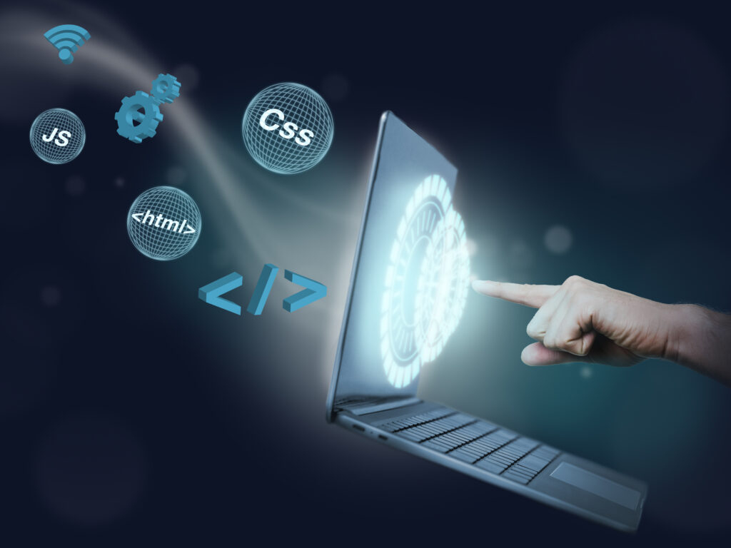 A hand interacting with a laptop's holographic interface showing web development icons like HTML, CSS, and JS