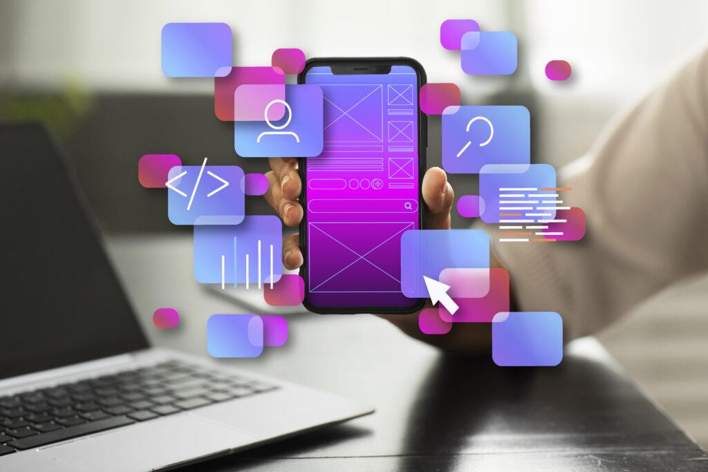 Person holding a smartphone displaying app UI design elements, with floating icons representing app development and user interface design, next to a laptop