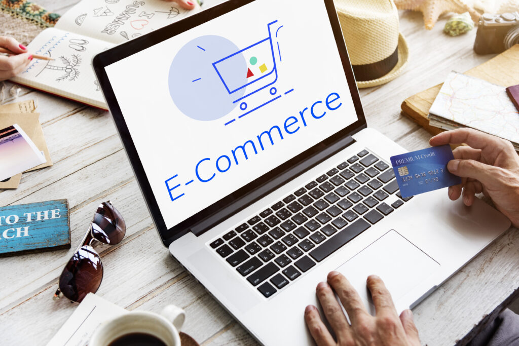 A person holding a credit card to make a payment on a laptop with an 'E-commerce' shopping cart graphic on the screen