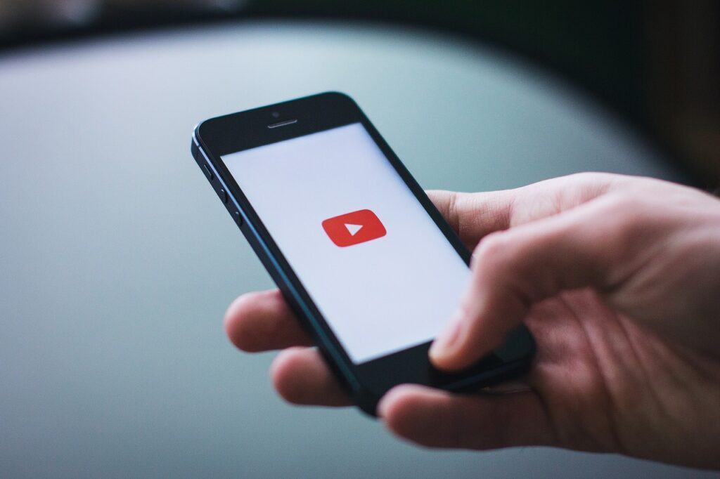 Hand holding a smartphone with the YouTube app loading screen – representing mobile video consumption and YouTube marketing engagement.