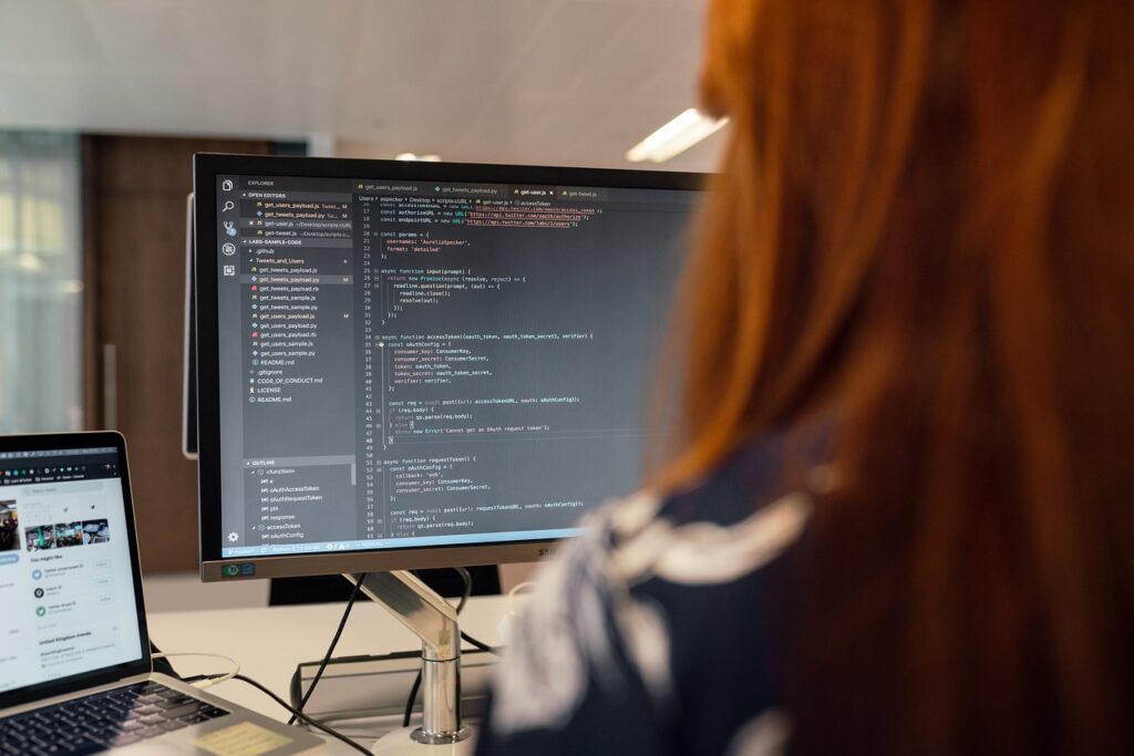 Software developer writing and reviewing code on a desktop monitor in a modern office