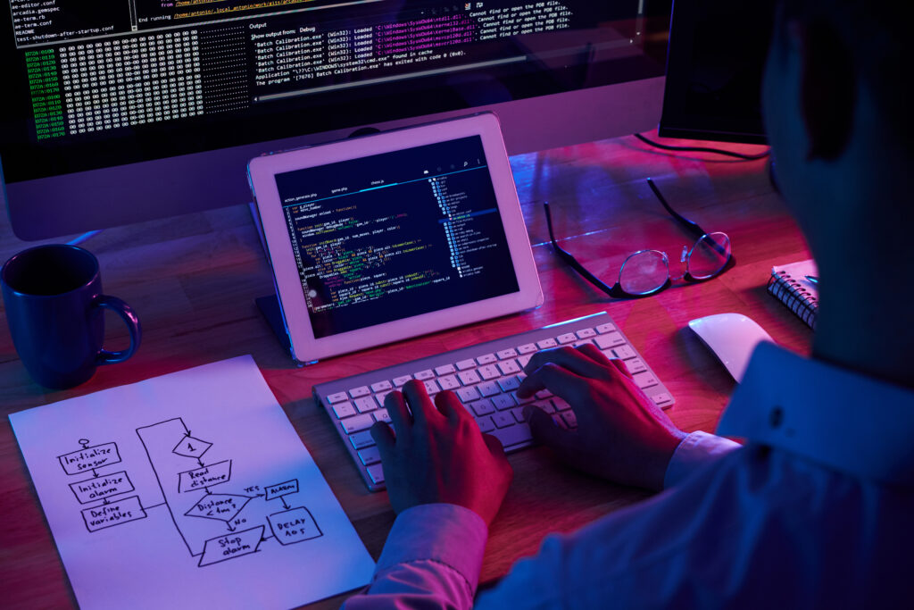 Developer writing code on a tablet with flowchart and debugging screen in the background.